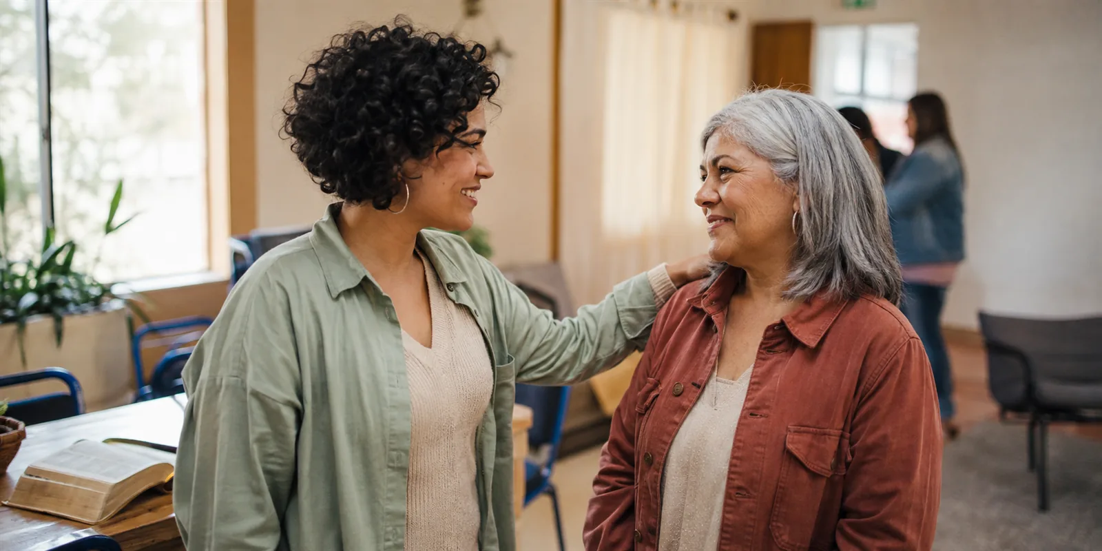 Dos mujeres conversando y sonriendo, una con la mano en el hombro de la otra